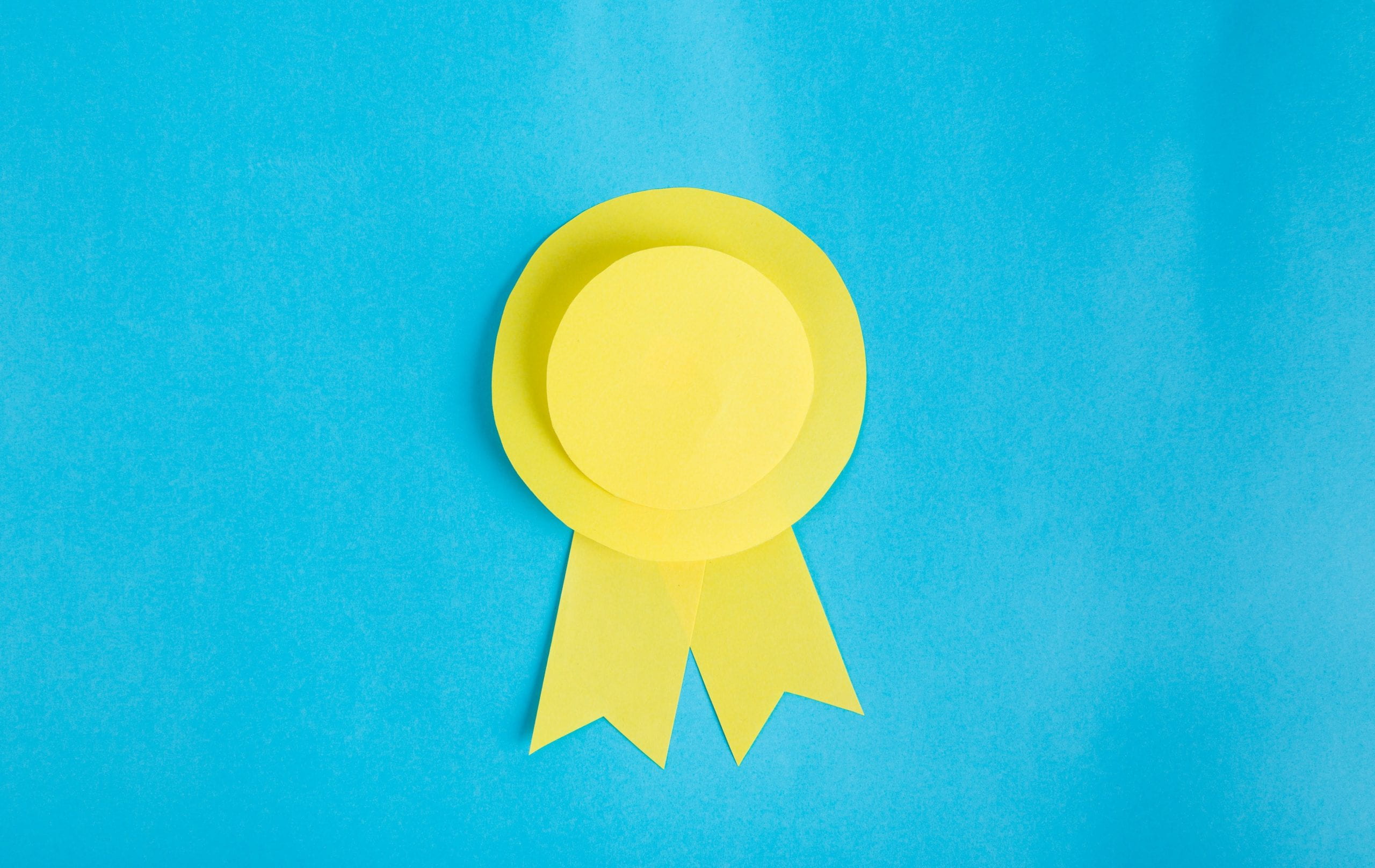 A yellow ribbon on a blue background to navigate to an article about Dr Polly Newcomb's award.
